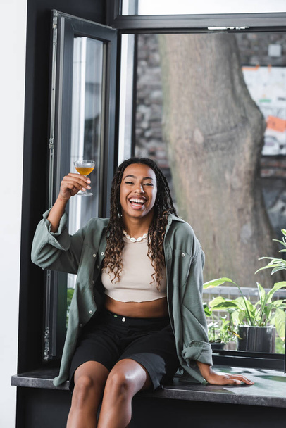 Excited african american woman holding cocktail near window in cafe  - Foto, Bild