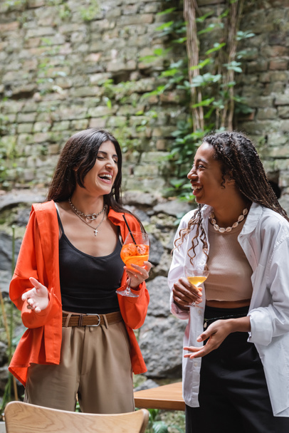 Happy multiethnic friends talking and holding cocktails on cafe terrace  - Fotó, kép