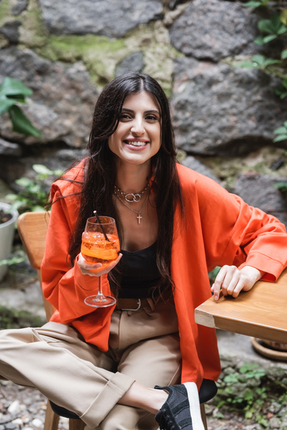 Positive woman holding cocktail and looking at camera on terrace of cafe  - Photo, Image