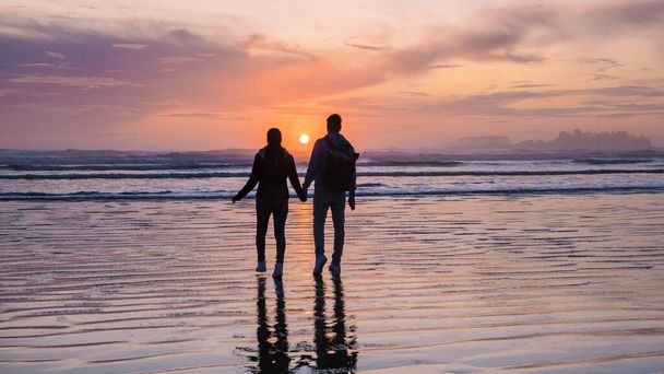 пара мужчин и женщин средних лет, наблюдающих закат на пляже канадского острова Тофино Ванкувер, красивый закат на пляже с розово-фиолетовыми цветами в небе. Канада Тофино-Ванкувер - Фото, изображение
