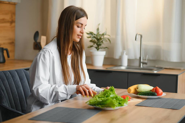 Beautiful young woman is preparing vegetable salad in the kitchen. Healthy Food. Vegan Salad. Diet. Dieting Concept. Healthy Lifestyle. Cooking At Home - Fotoğraf, Görsel