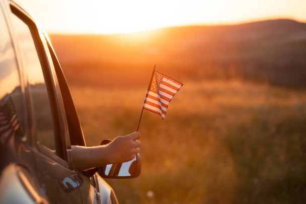 Man holding an American flag on a road trip. Independence Day or traveling in America concept. - Foto, Imagem