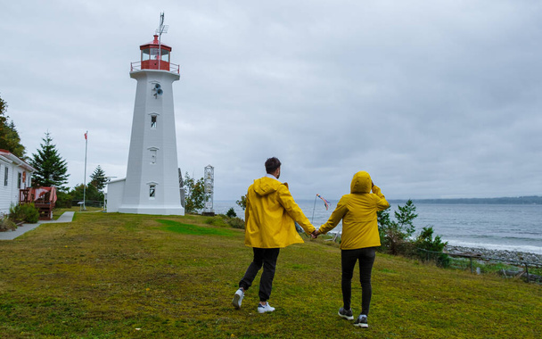 Quadra Island old historical lighthouse at Cape Mudge Vancouver Island, Canada. couple in yellow raincoats during the storm by the coast of Vancouver Island.  - Photo, Image