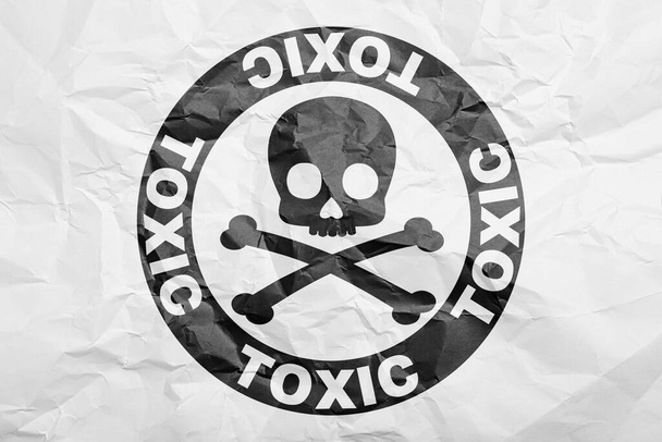 Hazard warning sign (skull-and-crossbones symbol and word TOXIC) on crumpled white paper, top view - Foto, Imagen