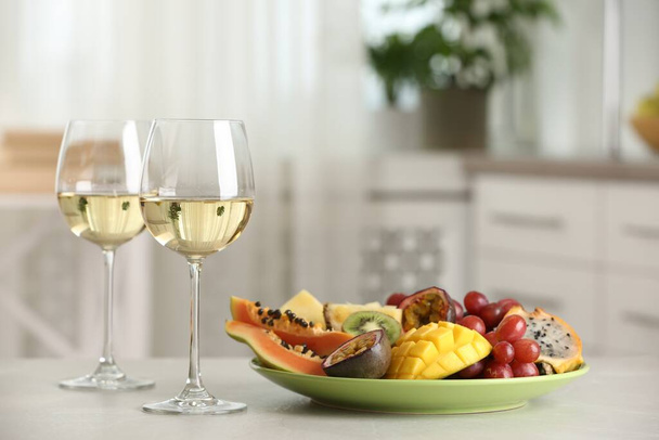Delicious exotic fruits and glasses of wine on white table indoors - Valokuva, kuva