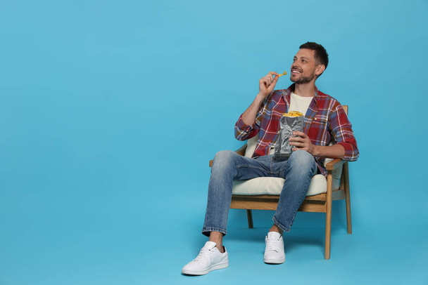 Handsome man eating potato chips on light blue background, space for text - Foto, immagini