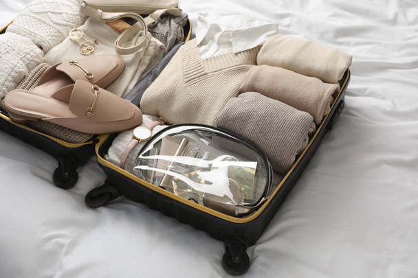 Open suitcase with folded clothes, shoes and accessories on bed - Zdjęcie, obraz