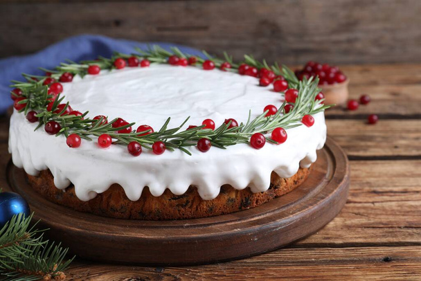 Traditional Christmas cake decorated with rosemary and cranberries on wooden table, closeup - Fotoğraf, Görsel
