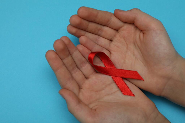 Little girl holding red ribbon on blue background, closeup. AIDS disease awareness - Φωτογραφία, εικόνα