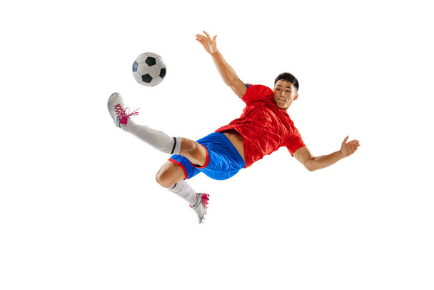 Portrait of young man, football player in motion, training, kicking ball in jump isolated on white studio background. Final winning goal. Concept of sport, team game, action, motion. Copy space for ad - Foto, imagen