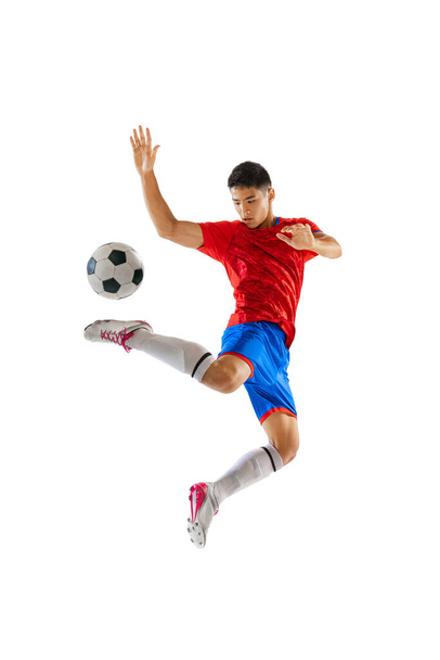 Portrait of young man, football player in motion, training, kicking ball in a jump isolated over white studio background. Concept of sport, team game, action, motion. Copy space for ad, poster - Zdjęcie, obraz