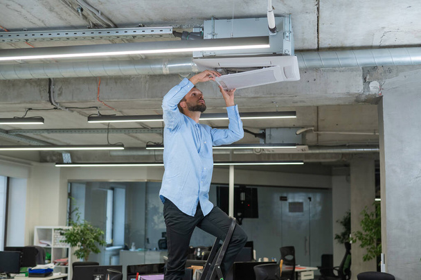 Caucasian bearded man repairing the air conditioner in the office - Foto, Bild