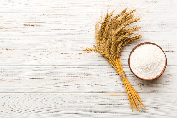 Puesta plana de harina de trigo en tazón de madera con espiguillas de trigo sobre fondo de color. crisis mundial del trigo. - Foto, Imagen