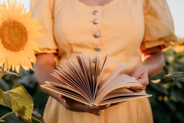 Woman flips through pages of old paper book on sunflowers field background. Aesthetics scene. Education, science, nature concept. High quality photo - Φωτογραφία, εικόνα