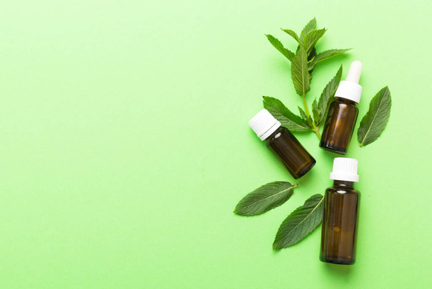Natural Mint Essential Oil in a Glass Bottle. organic cosmetics with herbal extracts of mint on colored background. - Photo, Image