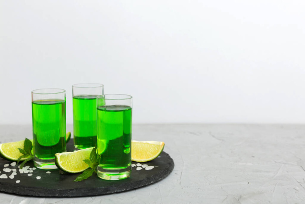 Sweet refreshing mint liqueur, with ice and mint leaves on table background, Shots with lime slice and mint flat lay. - Fotoğraf, Görsel