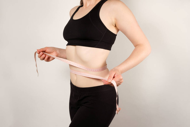 Eine Frau misst den Bauchumfang mit einem zentimetergroßen Klebeband in Großaufnahme. Schlankheitskonzept. - Foto, Bild
