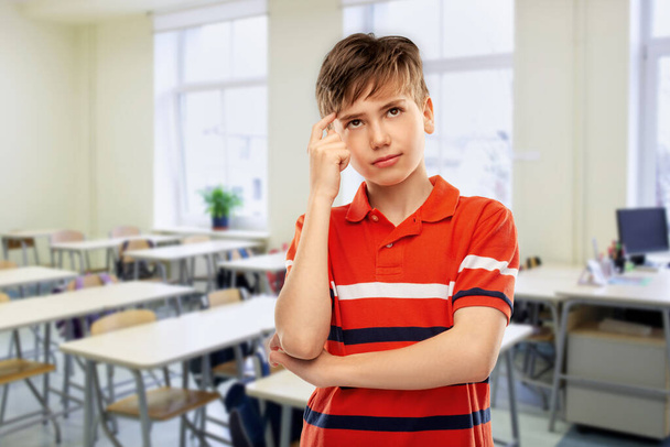 school, education and people concept - thinking student boy in red polo t-shirt over classroom background - Fotoğraf, Görsel