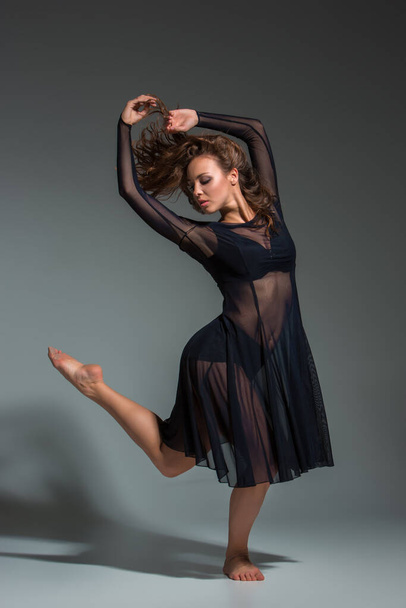 Χορεύτρια με μαύρο φόρεμα. Σύγχρονος μοντέρνος χορός σε γκρι φόντο. Γυμναστική, τεντωμένο μοντέλο - Φωτογραφία, εικόνα