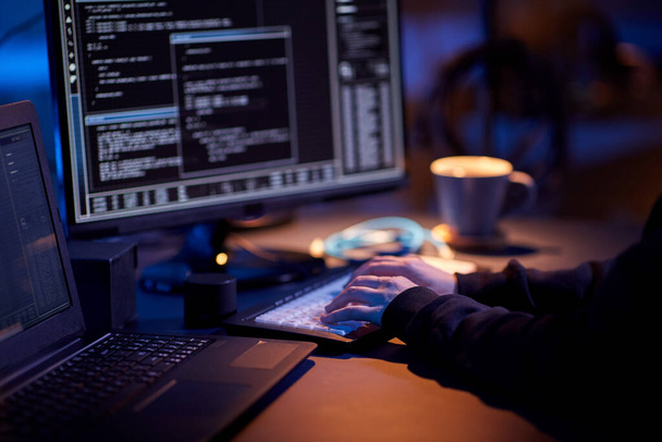 cybercrime, hacking and technology concept - close up of hacker in dark room writing code or using computer virus program for cyber attack - Foto, Imagem