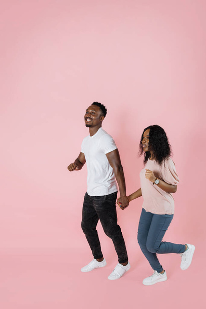 Full length shot of a african american man and woman in casual outfit walking or running together isolated on pink background. - Foto, afbeelding