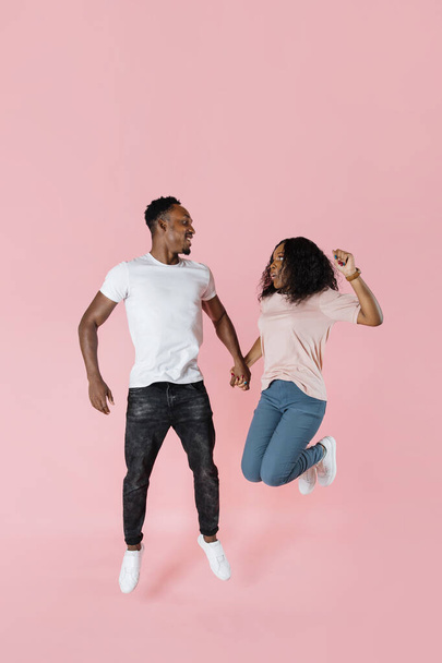 Повнометражний знімок стрибків африканської пари, що розважаються разом. Студійне фото молодих людей на рожевому фоні, копіювання простору
. - Фото, зображення