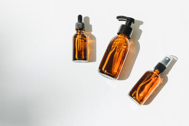 A group of amber bottles on an white table with face care products. A set of cosmetics in a glass package. Top view - Foto, Imagen