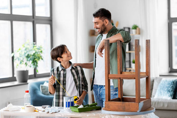 family, diy and home improvement concept - happy smiling father and son with ruler restoring old table at home - Фото, изображение