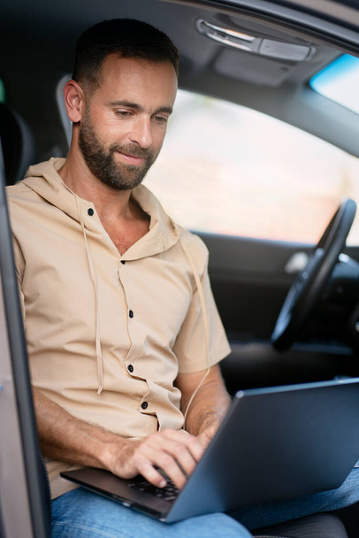 Handsome hispanic man using laptop computer working online sitting in car - 写真・画像