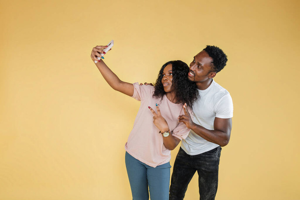 Joyful people using mobile phone to take selfies together in studio. African man and woman taking picture with smartphone and having fun in front of camera. Carefree couple feeling happy. - Photo, image
