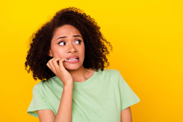 Photo of scared shocked girl dressed green t-shirt looking empty space biting fingers isolated yellow color background. - Φωτογραφία, εικόνα