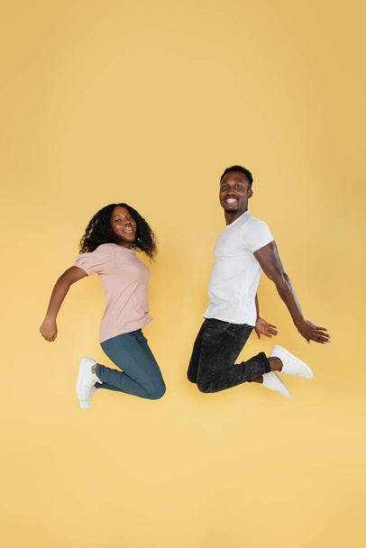 Full length shot of jumping african couple having fun together. Studio photo of young people on yellow background, copy space - Fotó, kép