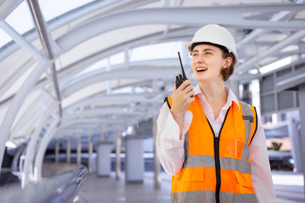 Caucasian woman engineer is using walkie talkie while inspecting the construction project for modern architecture and real estate development - Zdjęcie, obraz