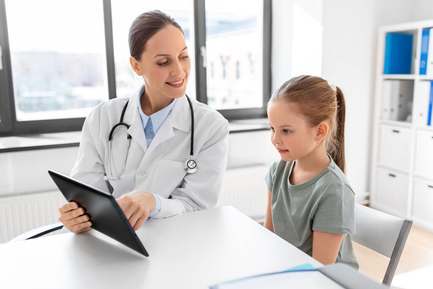 medicine, healthcare, pediatry and people concept - female doctor or pediatrician showing tablet computer to little girl patient at clinic - Фото, изображение