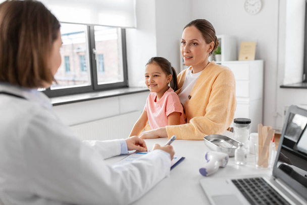 medicine, healthcare and pediatry concept - happy smiling mother with little daughter talking to doctor at clinic - Foto, Imagem