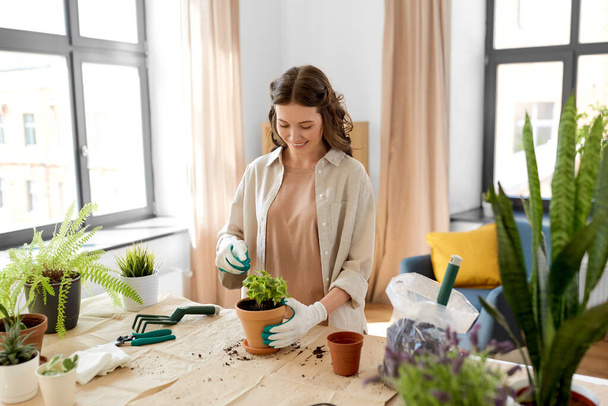 people, gardening and housework concept - happy woman in gloves with spray planting pot flowers at home - Foto, afbeelding