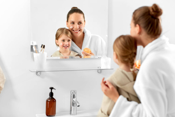beauty, family and people concept - happy smiling mother and daughter with moisturizer in bathroom - Fotografie, Obrázek