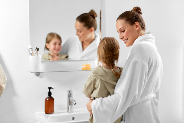 beauty, hygiene and people concept - happy smiling mother and daughter looking to mirror in bathroom - Fotografie, Obrázek