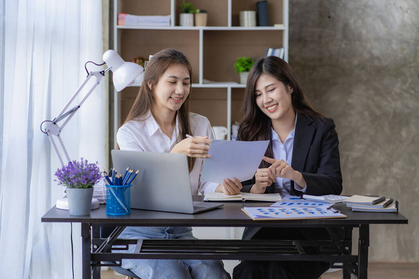 Two Asian women with laptop and financial graphs calculating accounting and taxes at the office. business idea - Foto, Imagem