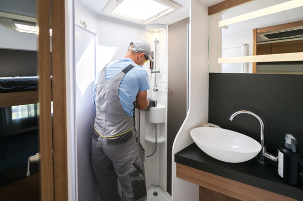 Rear View of Caucasian Worker in Grey Uniform Repairing the Hand Shower in Recreational Vehicle Bathroom. RV Care and Maintenance Theme. - Φωτογραφία, εικόνα