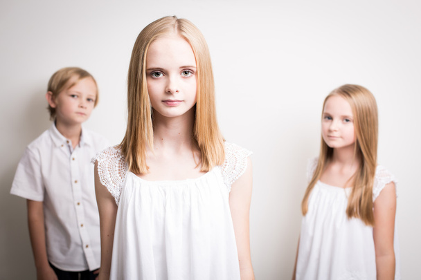 Kaksi sisarta ja heidän veljensä pukeutunut valkoinen studiossa
 - Valokuva, kuva