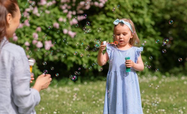 család, anyaság és emberek koncepciója - boldog anya kislányával szappanbuborékokat fúj a nyári parkban vagy a kertben - Fotó, kép