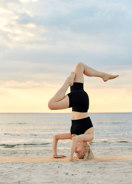 fitness, sport, and healthy lifestyle concept - woman doing yoga headstand on beach over sunset - Фото, зображення