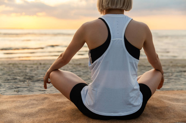 yoga, mindfulness and meditation concept - woman meditating in lotus pose on beach over sunset - Foto, Imagen