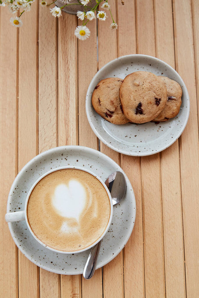No sugar, natural, homemade cranberry cookies on the plate, cappuccino in white ceramic cup on wooden table top view. Aesthetic breakfast at the cafe terrace outside with blurred foreground - 写真・画像