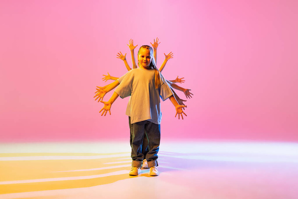 Modern choreography lesson. Dance group of happy, active little girls in t-shirts and jeans in action isolated on orange background in neon. Concept of music, fashion, art, childhood, hobby. - Photo, image