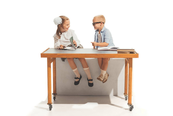 Portrait of little boy and girl, children sitting at desk and studying, doing homework isolated over white background. Concept of childhood, game, school, fun, education. Copy space for ad - Foto, immagini