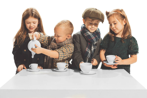 Portrait of beautiful children, boys and girls in stylish autumn clothes isolated over white studio background. Tea party. Concept of childhood, game, school, fun, education. Copy space for ad - Фото, изображение
