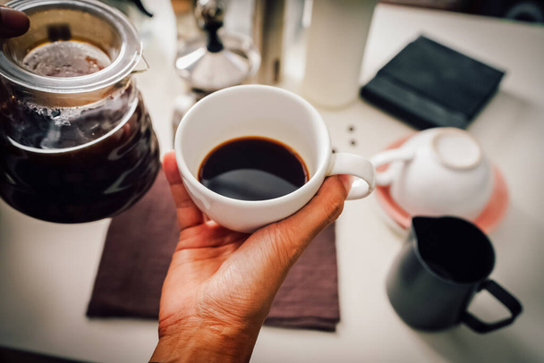 Закройте руку наливая кофе капает в кувшин в белый стакан с оборудованием, инструмент пивоварения с оборудованием на кухне дома на белой кухне дома - Фото, изображение