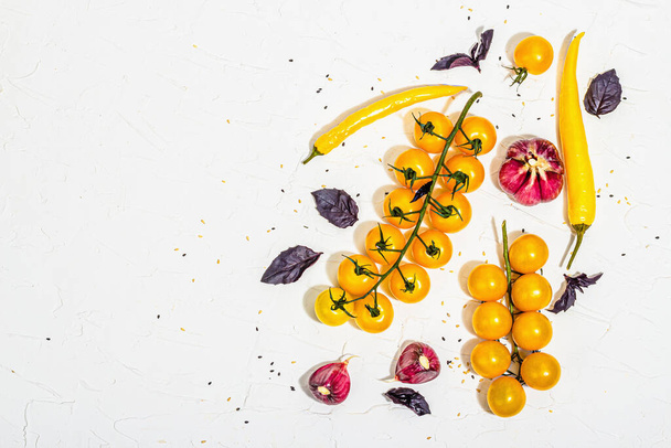 Culinary background with ripe vegetables. Yellow tomato cherries, chili pepper, garlic, purple basil. Fresh vegetables on white putty background, modern hard light, dark shadow, flat lay, top view - Fotó, kép